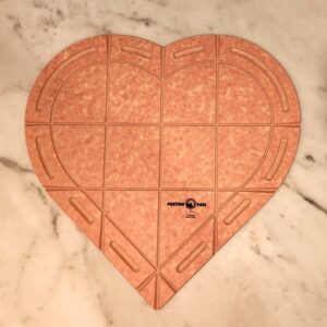 heart shaped composite board with a heart shaped groove inside. Three vertical lines and two horizontal lines to mark grooves for cutting. grooved handles around the edges for easy carrying.